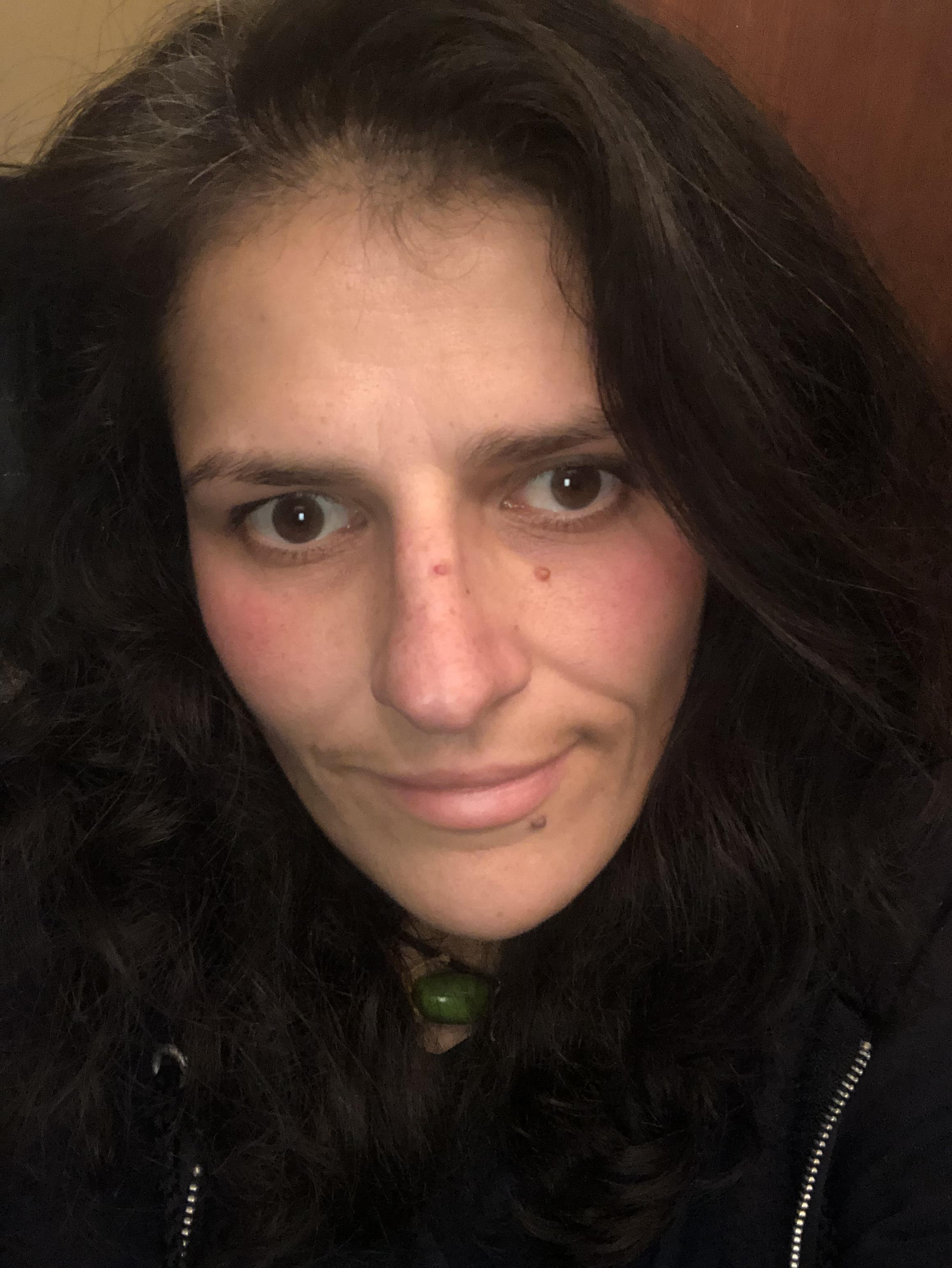 Paulina poses for the camera with dark brown long hair framing her face, wearing a black hoodie and a teal pendant necklace.