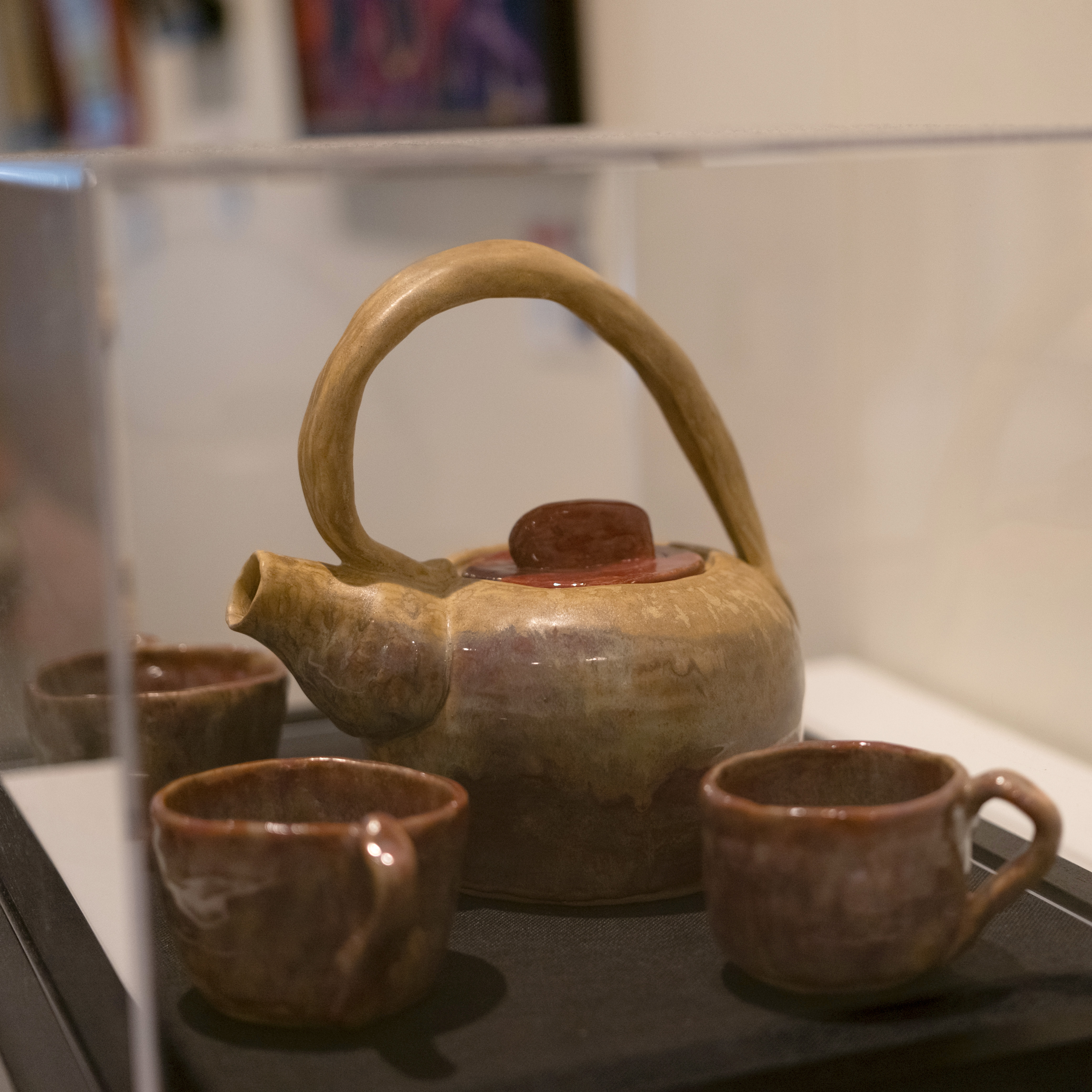 A ceramic, hand-crafted tea set sits in a glass case. This is 2024 Creative Power Award winner by Richard Berkholtz.